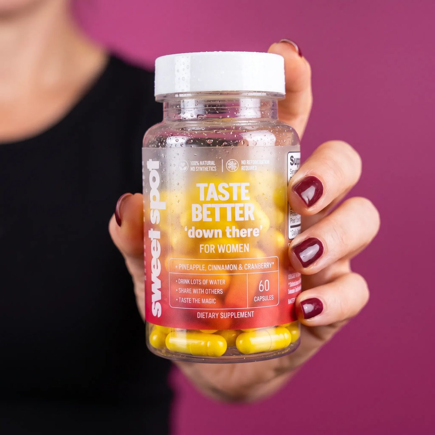 A hand holds the Taste Better For Women bottle against a magenta wall.