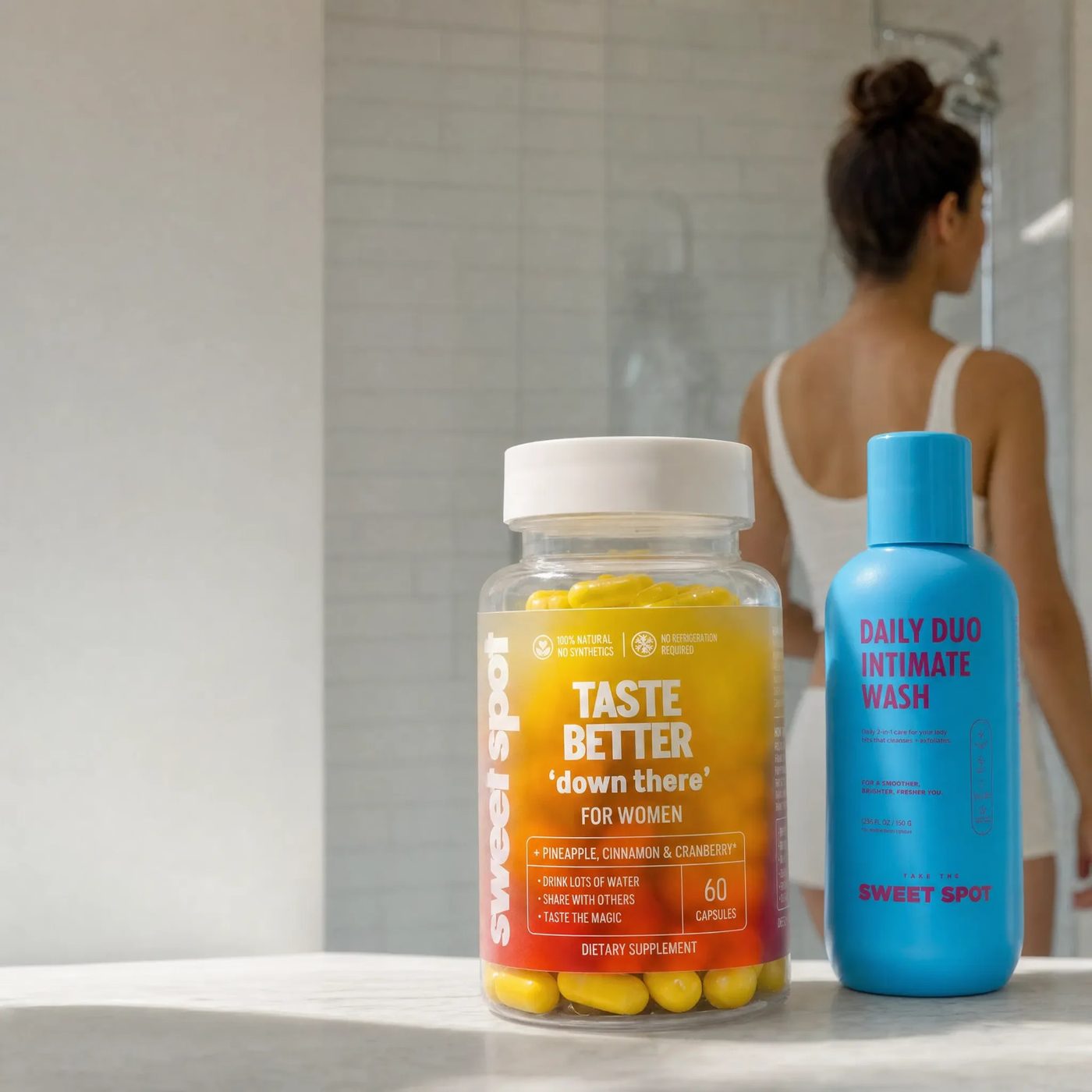 For Women capsules and Daily Duo wash on a bathroom counter, woman in the shower beyond.
